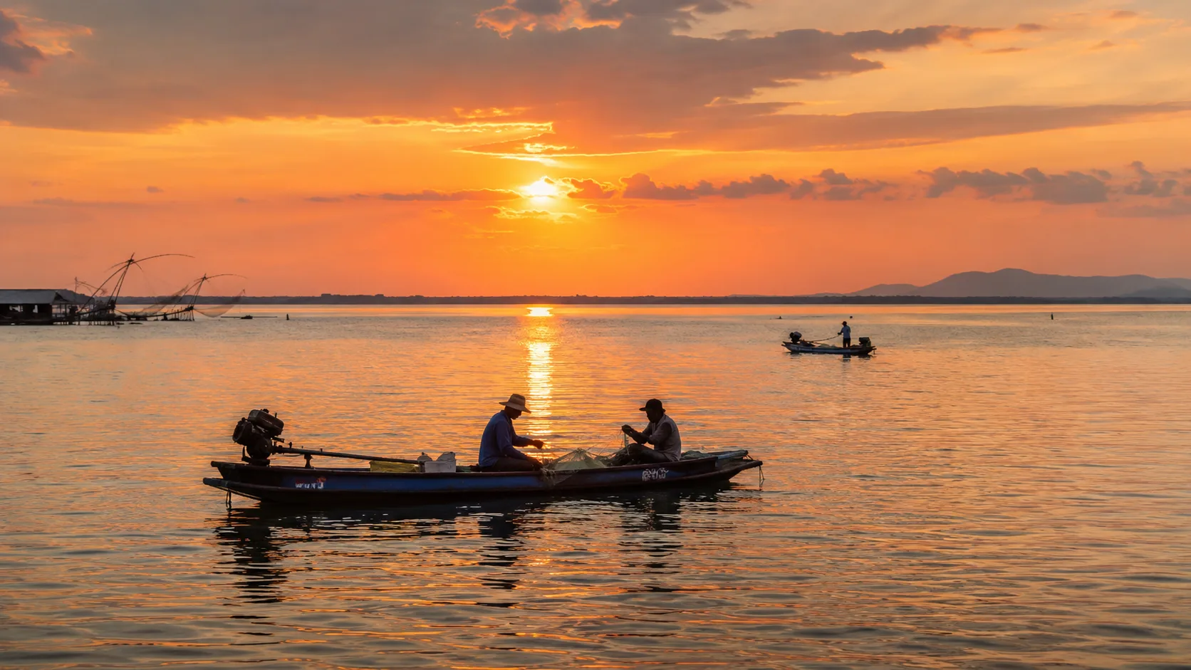 Fishing boats crossing Nong Han Lake during a warm sunrise.